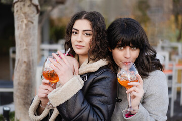 Young couple of girlfriends drinking Aperol Spritz cocktail outdoors looking at the camera
