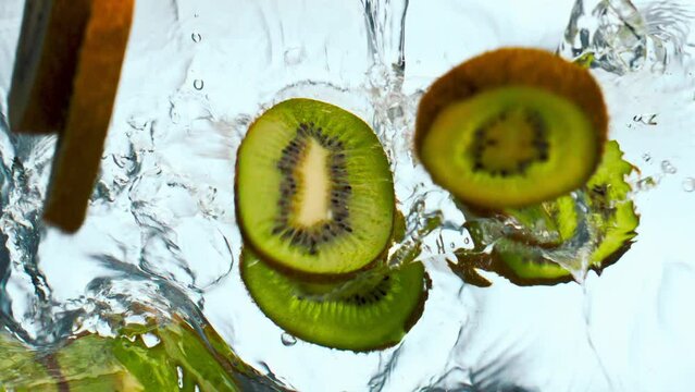 Slices kiwi falling water in super slow motion close up. Fruit dropped in liquid