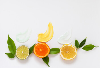 Close-up texture of samples of three types of vitamin anti-aging facial skin creams with extracts of lime, tangerine and lemon on white background. Chopped fruits nearby. Flat lay, mock up, top view