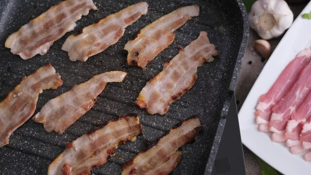 cooking Pieces of flavorful sliced organic bacon fried in a grill pan