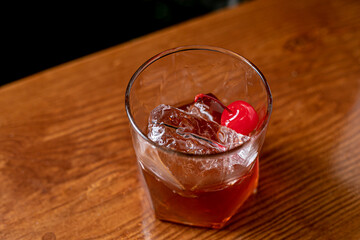 Old-fashioned drink at bar with a slice of orange, cherry and ice, a classic alcoholic drink