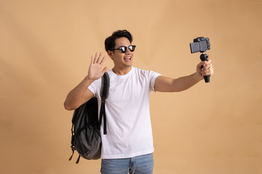 Young Asian tourist backpacker man smiling and taking a selfie and blog isolated on beige background