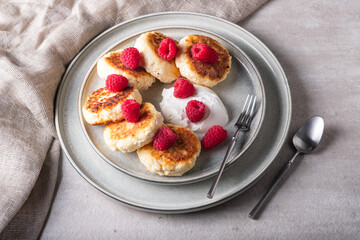Cheesecakes or syrniki on a round plate with raspberry, sour cream and raspberry syrup.Healthy breakfast. Delicious dessert.