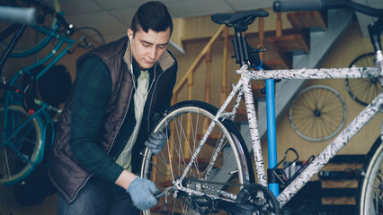 Experienced mechanic in gloves is assembling bicycle adjusting back wheel during servicing vehicle...