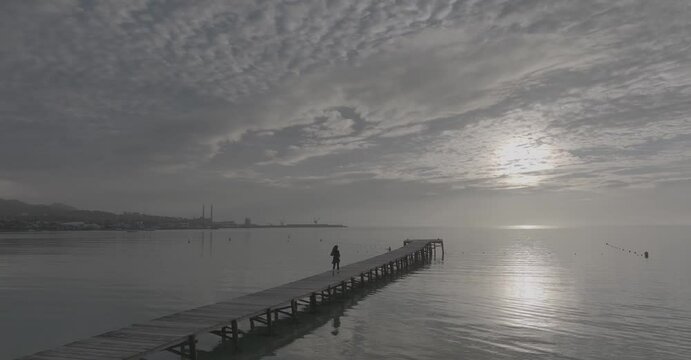 Mujer corre por la playa amanecer con muelle de fondo y palmeras 50fps (Formato D-log para edici&oacute;n y correcci&oacute;n de color profesional)