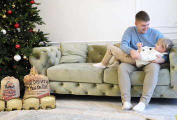 Father and son have fun together in a living room decorated with Christmas decor. Father tickling son