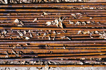 Top view old rusted iron bars and dry leaves on floor. Close up to stack of straight old rusty steel reinforcement structural steel bars from construction site. Steel rod with rust. Rusty Metal Bars.