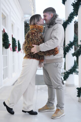 A fashionable married couple, a man and a woman, pose on the porch of their house. Couple hugging and kissing