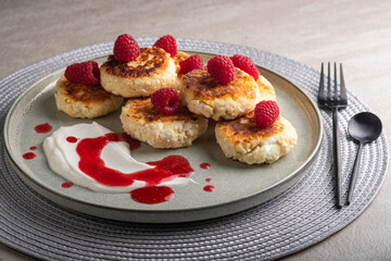 Cheesecakes or syrniki on a round plate with raspberry, sour cream and raspberry syrup.Healthy breakfast. Delicious dessert.
