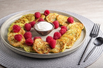Gluten-free zucchini pancakes with fresh raspberries, raspberry jam, sour cream on a round grey plate.  Healthy food concept, summer food.