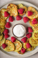 Gluten-free zucchini pancakes with fresh raspberries, raspberry jam, sour cream on a round grey plate.  Healthy food concept, summer food.