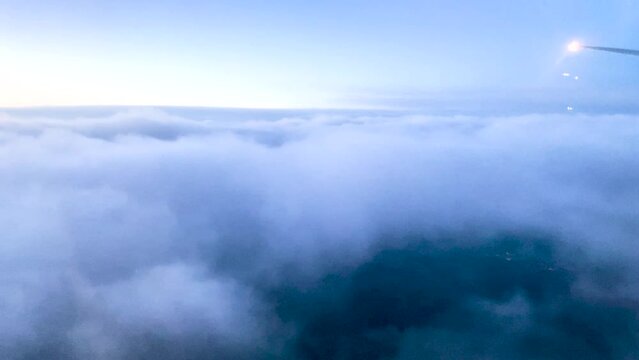 Plane descending through thick blue clouds at blue hour. View of sea of clouds from airplane window. 