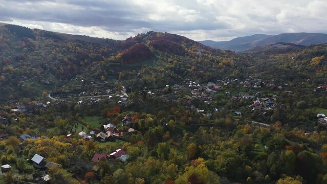 Aerial orbit shot over an old village during autumn, showcasing colorful forests with autumn collors during morning sunlight