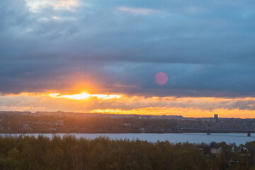 Sunrise over the city across the river. Panoramic View. Colorful sky with sun in clouds.