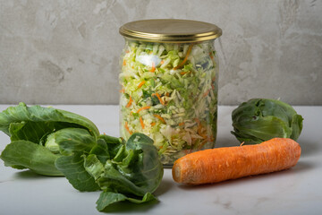 Homemade sauerkraut in a glass jar on a gray table.Cut green cabbage and carrots for cabbage soup.