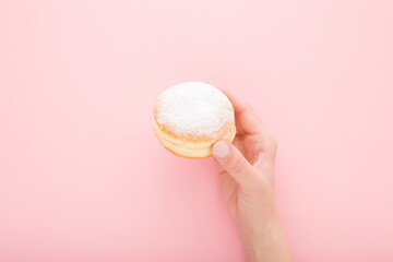 Young adult woman hand holding fresh donut with sprinkled sugar on light pink table background....