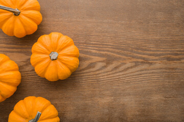 Fresh orange small pumpkins on dark brown wooden table background. Closeup. Empty place for text. Top down view.