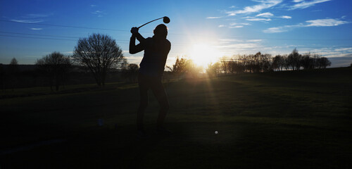 A man plays golf at sunset ...
