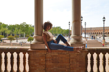 Beautiful woman is sightseeing in seville, the woman is sitting between two columns in the biggest and most famous square in seville. The woman is happy. Holiday and travel concept.