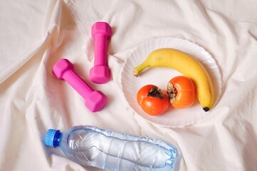 Pink dumbbells, fruit plate and water bottle. Healthy nutrition and workout at home. Flat lay photography, top view image - Powered by Adobe