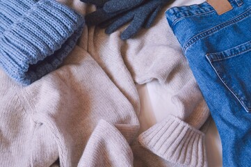 Fototapeta na wymiar Blue knitted hat, beige woolen sweater, jeans and gray gloves. Fall and winter clothes for cold weather