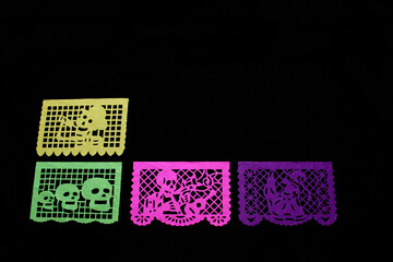 Colored papel picado for an offering for the Mexican tradition of the Day of the Dead and All Saints with skull shapes on a black background