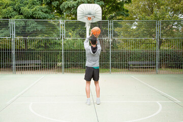 Man throwing a ball from the three-point line on an outdoor basketball court.