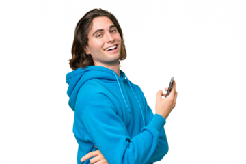 Young handsome man isolated on green chroma background holding a mobile phone and with arms crossed