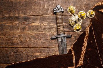Ancient sword and burning candle on the wooden table flat lay background with copy space.