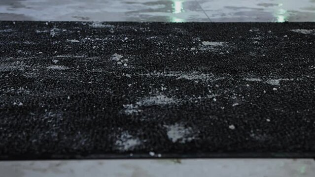 People wipe and shake snow covered shoes on fleecy rug mat at entrance to building. Safety from falling on slippery tiles. Customers go out and enter store from street outside. Exit from shopping mall