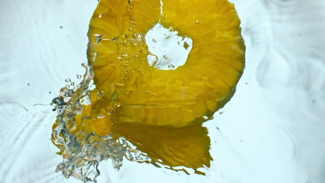 Yellow sliced pineapple splashing water close up. Juicy ananas falling in liquid