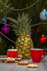 Pineapple, cup of coffee and a fir tree with Christmas ornaments on the background.
