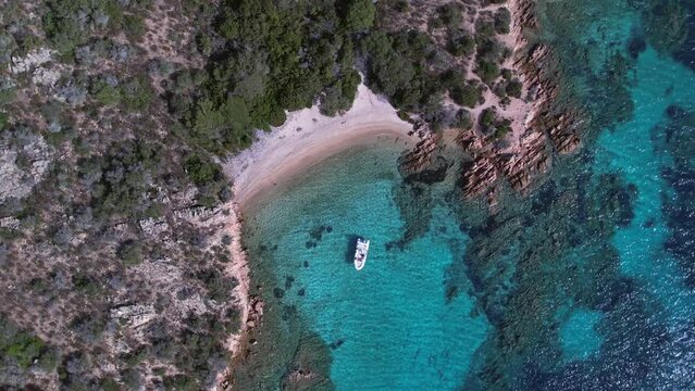 Aerial top down view of private yacht parked at coast of private beach amidst tall cliffs.