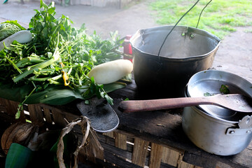 Outdoor kitchen cooking with large pots and pans and a selection of fresh vegetable and leafy green...