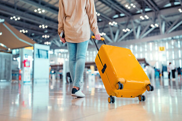 Young female traveler passenger walking with a yellow suitcase at the modern Airport Terminal, Back...