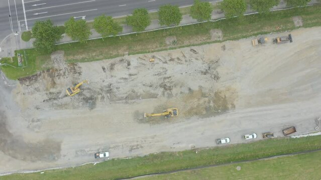 Smooth aerial decent looking down on excavators working together on empty construction site.