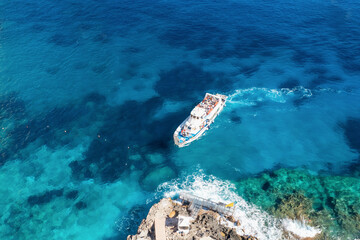 Aerial view beautiful seascape with stone dock and ship with tourists top view. Sea coast with blue, turquoise clear water on sunny day, aerial drone shot