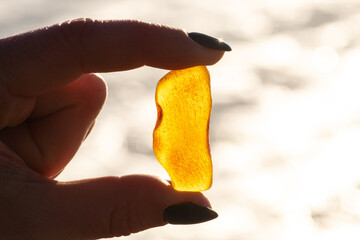 Beautiful big piece of yellow amber in the hand of a girl with water and sea waves on the background