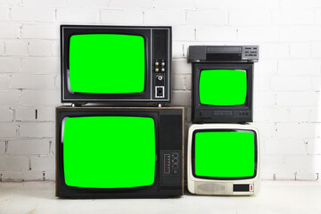 Four old vintage green screen televisions and a VCR stand against a white brick background.