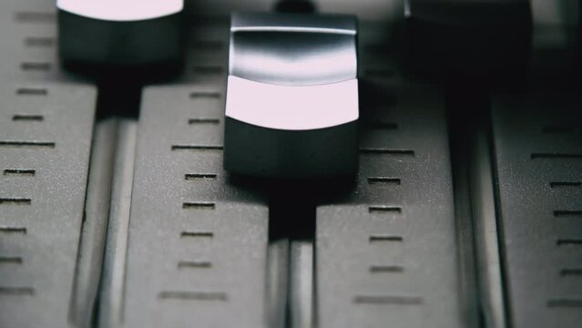 Main Mix Levels. Sound engineer is moving levers of a multitrack mixing console in the control room during a recording session.
