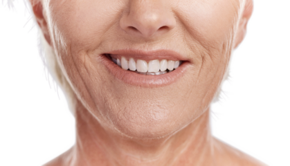 Happy mature caucasian woman with a bright smile, showing her natural looking veneers while posing against a purple copyspace background. Older woman happy with her oral hygiene while doing skincare