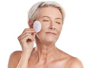 A mature caucasian woman using a cotton pad to remove makeup during a selfcare grooming routine. Older model  applying cleanser to her face against pink copyspace background