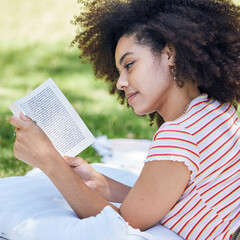 Black woman reading book, relax in park and picnic blanket with novel in nature. Education,...