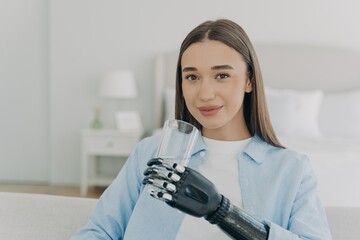 Smiling disabled girl holds glass with water by bionic prosthetic arm. Disability, healthy lifestyle