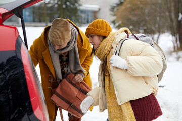 Side view portrait of young couple unloading car trunk in winter while travelling for Christmas holidays - obrazy, fototapety, plakaty
