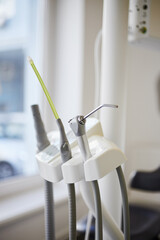 Compressed nozzle air and saliva ejector and other tools hoses on stand in dentist's office.