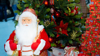 Santa Claus with a magic gift in his hands stands next to the Christmas tree.