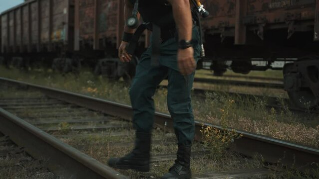 Bodybuilder with balloon drager on his back is training at railway yard and quickly pulls knees to chest leaning his hands on the rails