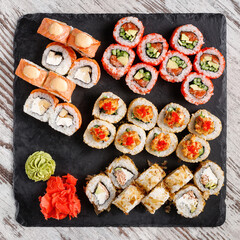 Large sushi set of various sushi rolls is served on black square metal slate.