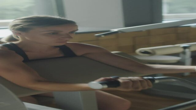 Vertical shot of strong woman using preacher machine while doing bicep curls in gym
